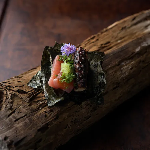 Close-up of an artfully plated dish with a vibrant green sauce, delicate garnishes, and edible flowers.