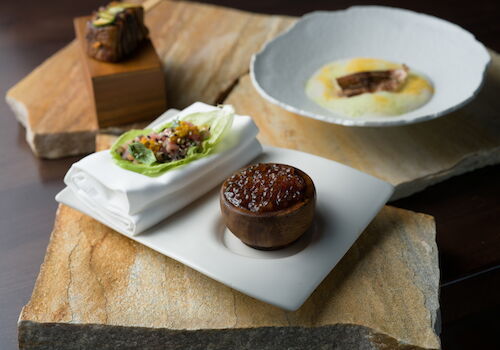 Artfully plated course with a delicate centerpiece and green garnish, presented on a white plate atop a wooden serving board