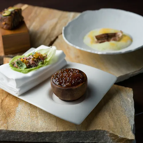 Artfully plated course with a delicate centerpiece and green garnish, presented on a white plate atop a wooden serving board