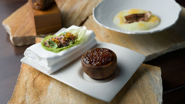Artfully plated course with a delicate centerpiece and green garnish, presented on a white plate atop a wooden serving board