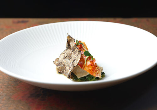 A gourmet dish featuring various ingredients on a white plate, artfully arranged with a dark background for contrast.