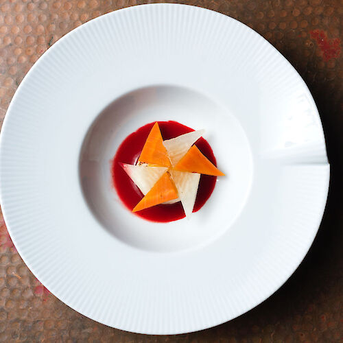 A white plate with an artistic dessert arrangement using colorful triangular elements on a red sauce.