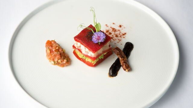 A plated gourmet entr&eacute;e: a red veggie-stacked terrine topped with a purple flower, plus sides of sauce and dark beans.