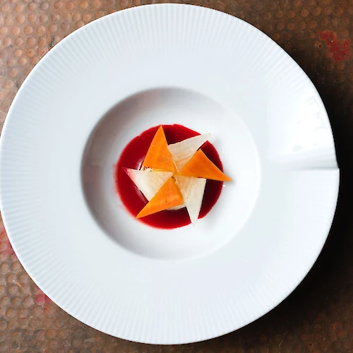 A white plate with an artistic dessert arrangement using colorful triangular elements on a red sauce.