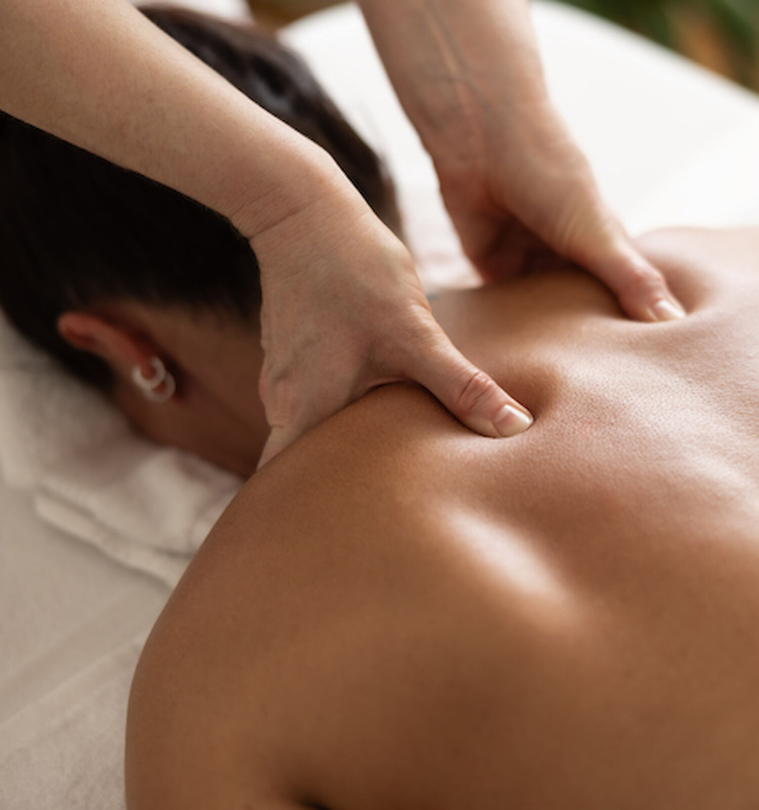 A person is lying face down receiving a back massage. The masseuse's hands are applying pressure on the person's upper back.