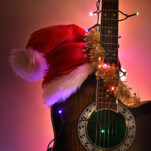 A guitar adorned with Christmas lights and tinsel, wearing a Santa hat, glowing warmly in colorful ambient light.