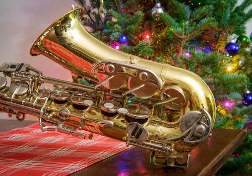A shiny gold saxophone lying on a table in front of a Christmas tree.