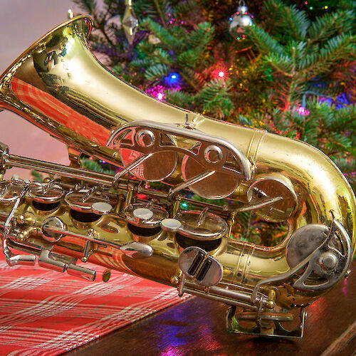 A shiny gold saxophone lying on a table in front of a Christmas tree.