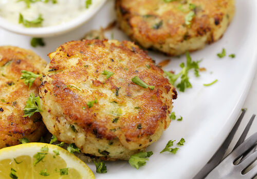 Delicious-looking golden brown potato or herb patties with herbs, lemon wedges, and a dipping sauce on the side, perfect for a fresh bite.