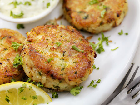 Golden pan-fried crab cakes with lemon wedges and a herb garnish, served with a creamy dip on the side.