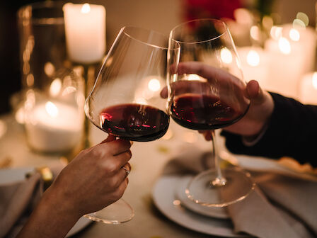 Two people clink wine glasses over a candlelit table, enjoying a romantic dinner setup with soft, warm lighting.