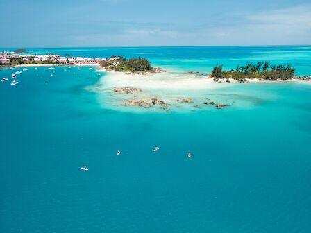 A tropical island with turquoise water, small rocks, and palm trees; boats dot the bay in a serene coastal scene.