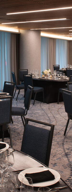 The image depicts an elegantly set dining area with round tables adorned with place settings, glassware, candles, and flower arrangements.