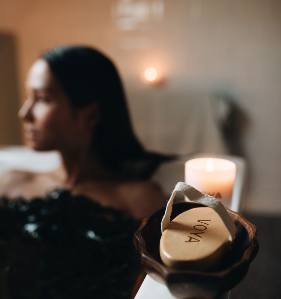 A cozy, dimly lit living room scene with a lit candle and a blurred woman relaxing behind it.