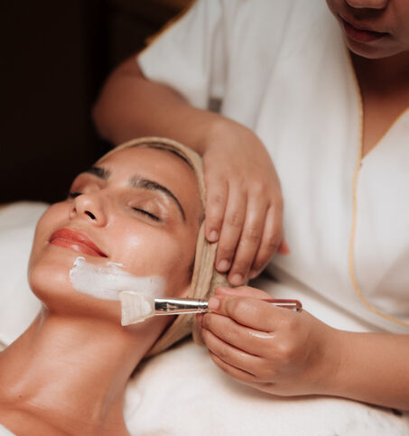Guest enjoying a relaxing facial treatment as a spa therapist applies a skincare mask.